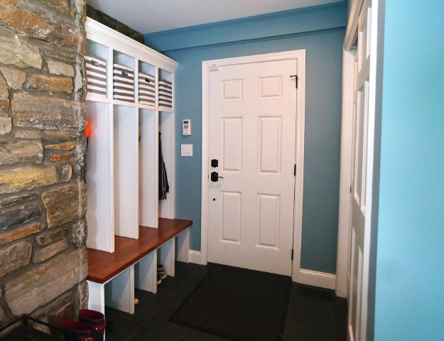 Mudroom with white lockers and shelves tucked behind stone wall.